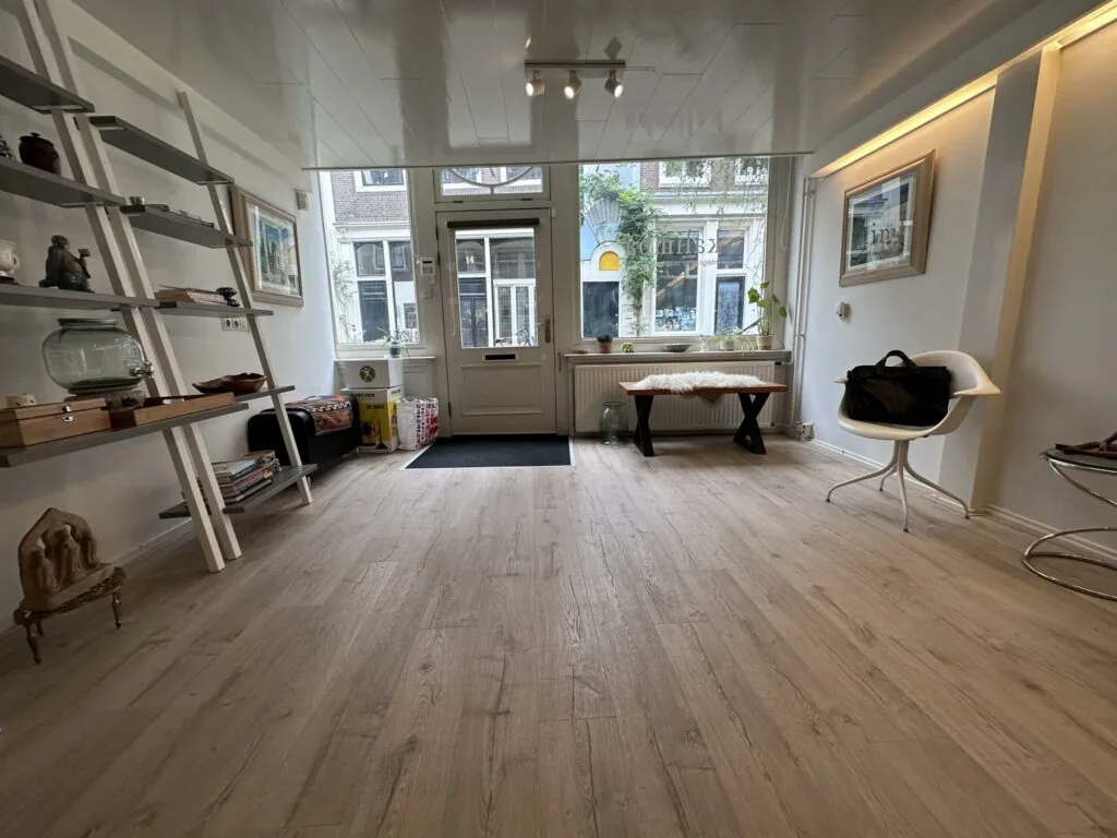 Moderne, lichte ontvangstruimte aan de Eerste Lindendwarsstraat met houten vloer, designmeubilair en grote etalageramen.